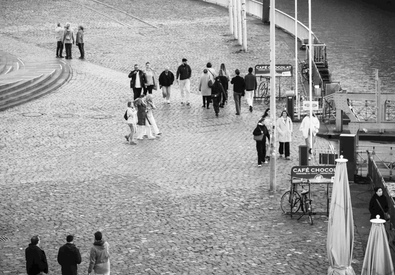 Menschen auf der Kölner Uferpromenade, Schwarz-Weiß-Aufnahme aus erhöhter Position.